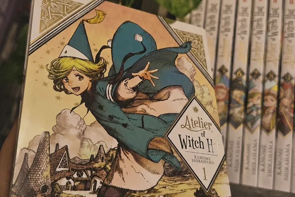 o volume 1 de witch hat atelier, de kamome shirahama, segurado na mão diante da estante